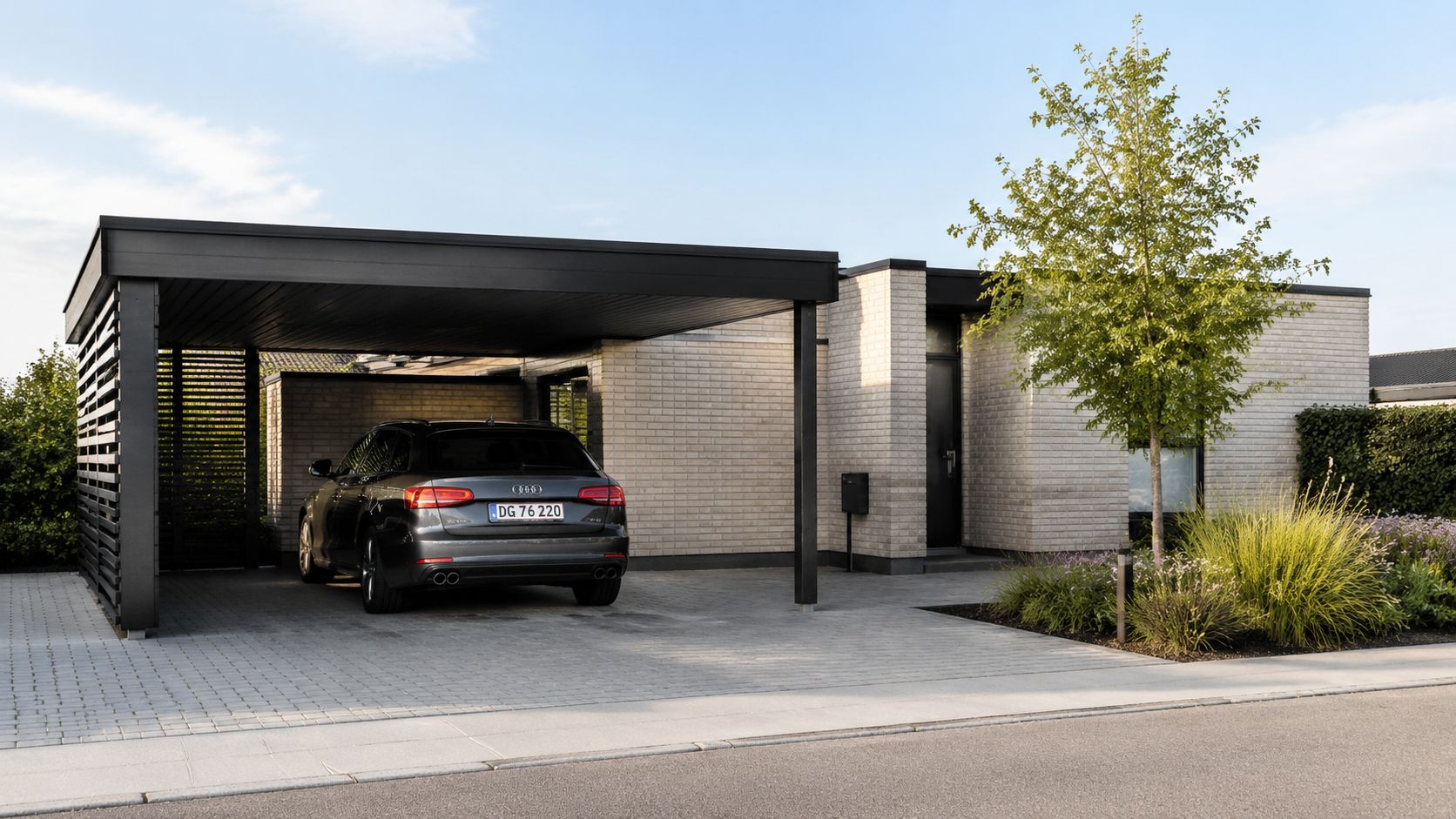En moderne muret villa med sort carport og en mørkegrå Audi parkeret foran huset på indkørslen.