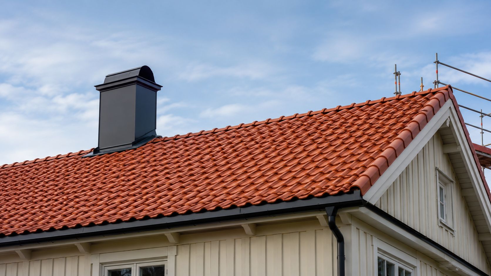 Et hus med nyt rødt tegltag, moderne skorsten og stillads i gang under en blå himmel.
